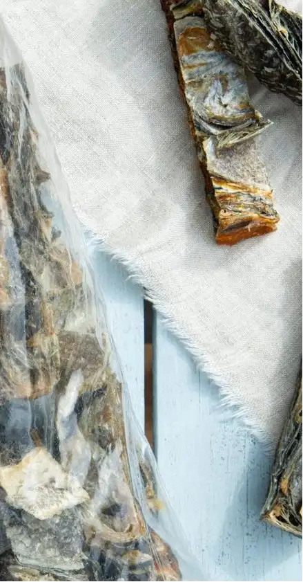 Dried fish, some in a clear plastic bag and others resting on a light-colored fabric surface.