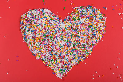 Heart-shaped sprinkles in vibrant rainbow colors on a red background.
