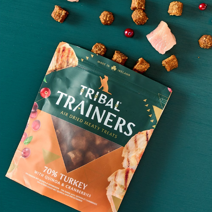 Packaging of Tribal Trainers dog treats on a teal background with treats scattered around.
