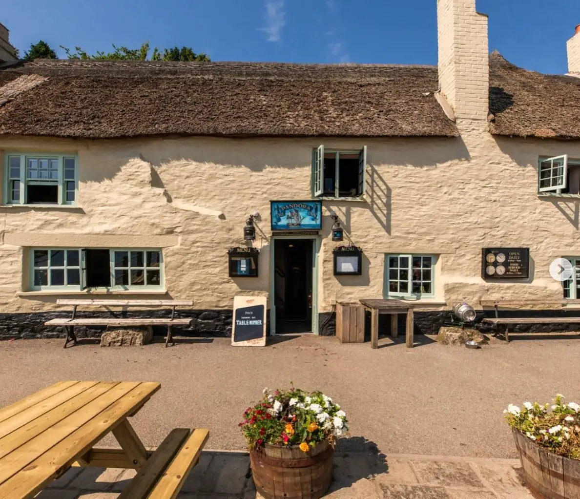 Charming Cornish village pub with cream thatched roof and picnic table