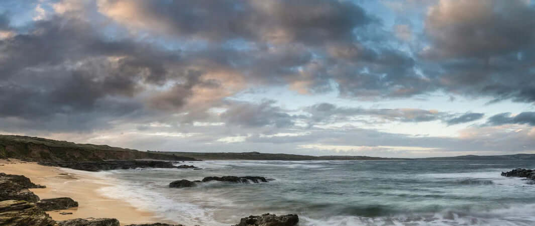 Gwithian Beach dog walk: sandy shore, rocky outcrop, crashing waves.