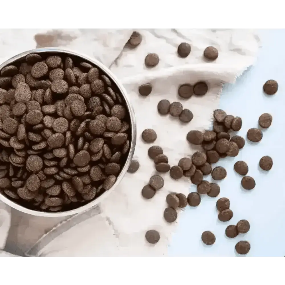 Chocolate chip cookie mix in a silver bowl with scattered chips on white cloth for grain free dog food