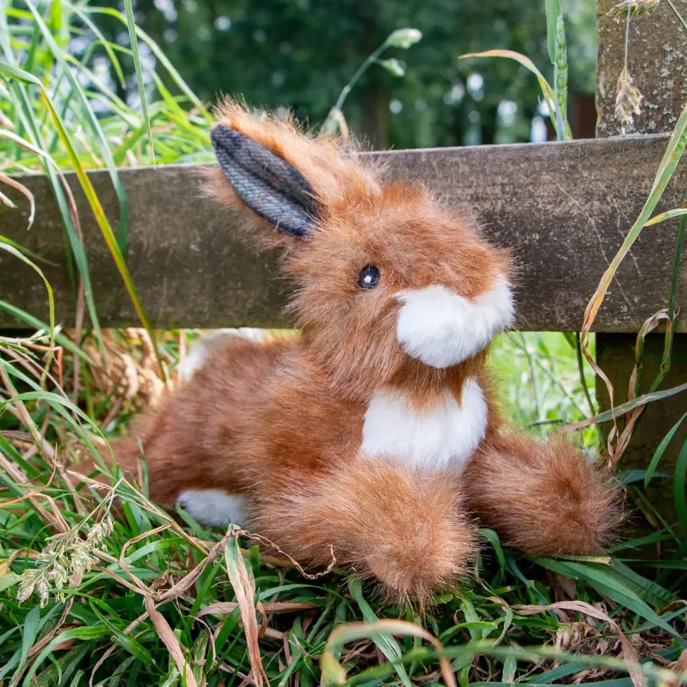 Plush toy fox sitting on grass next to a wooden fence