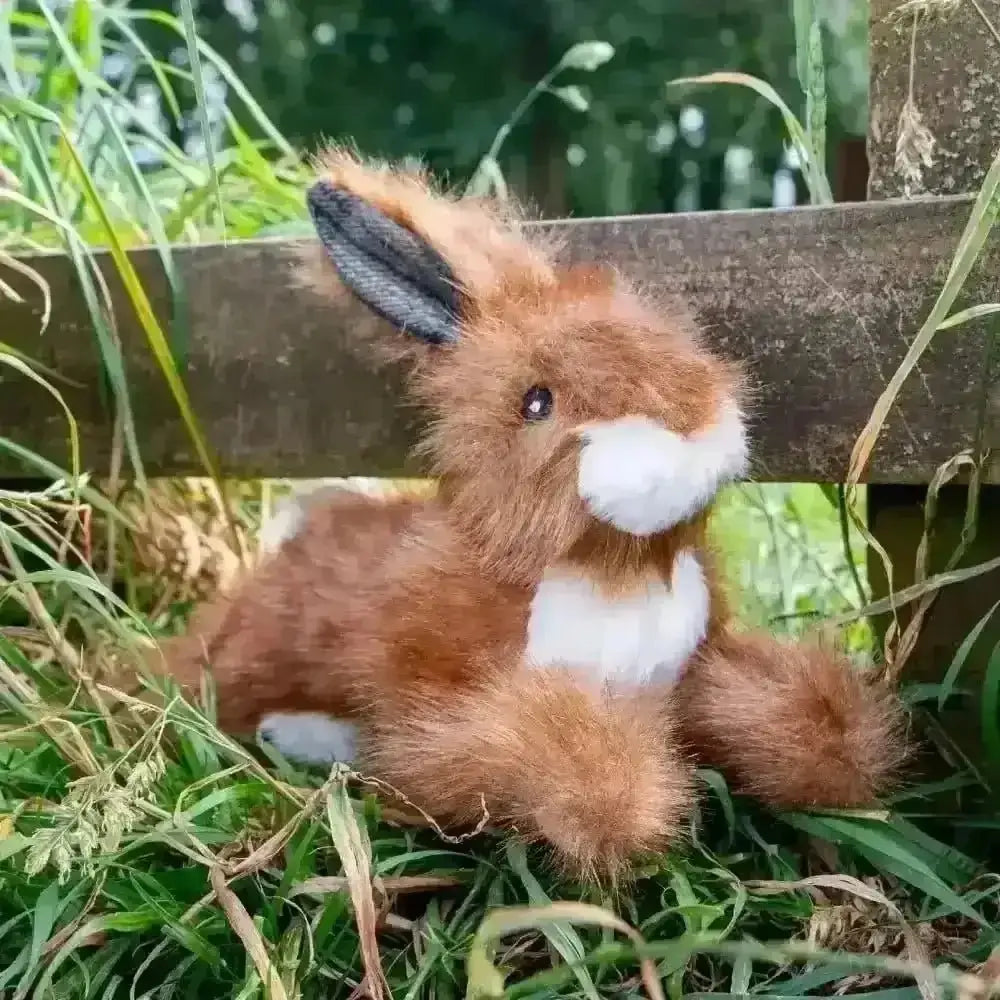 Plush toy fox sitting on grass next to a wooden fence