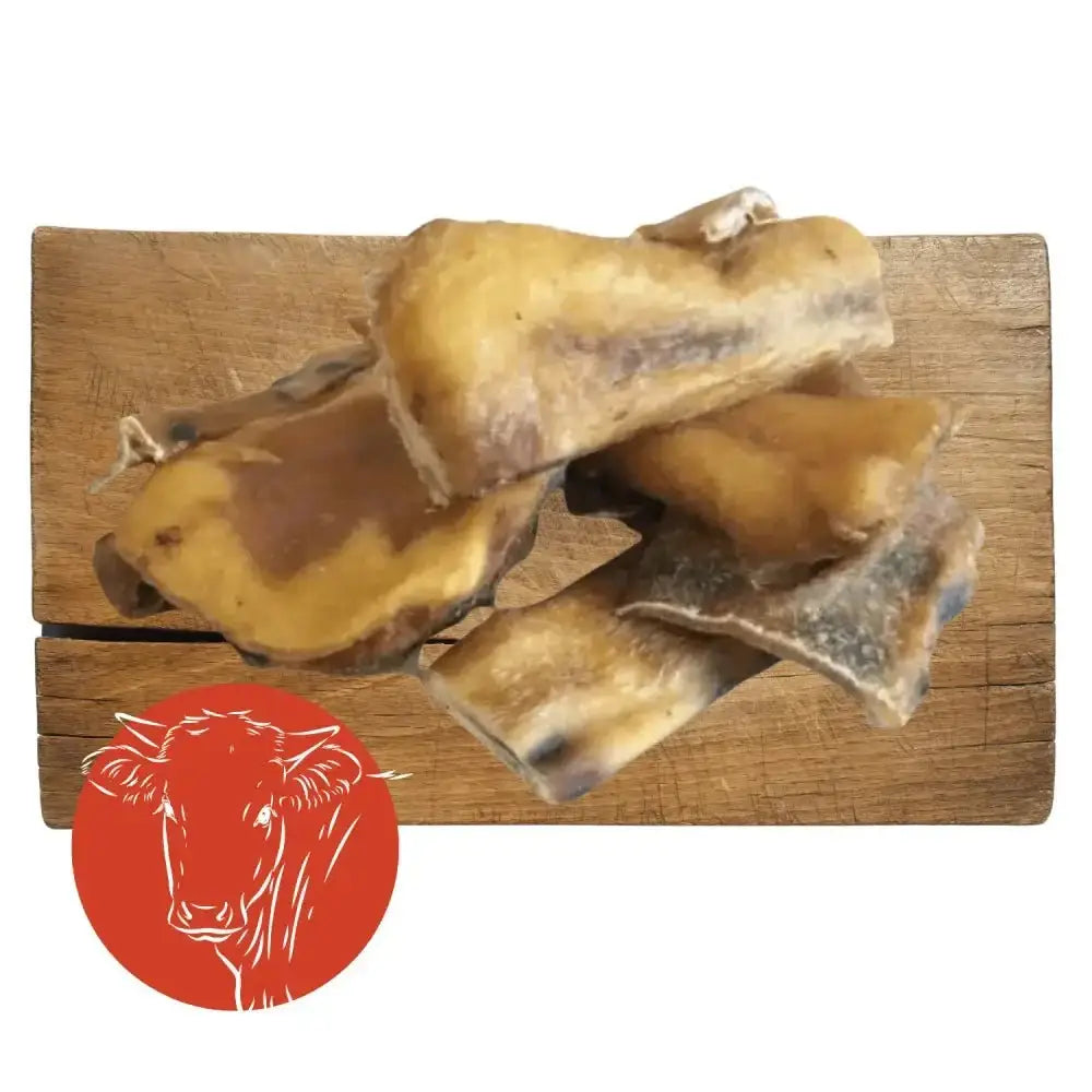 Goat bone dog chew toy with beef muscle pieces on wooden cutting board with red cow logo
