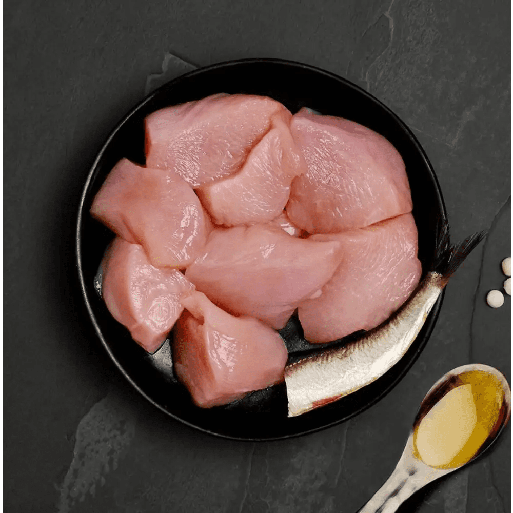 Black plate with raw chicken pieces, silver spoon, and salt shaker for Canagan Cat Food Can