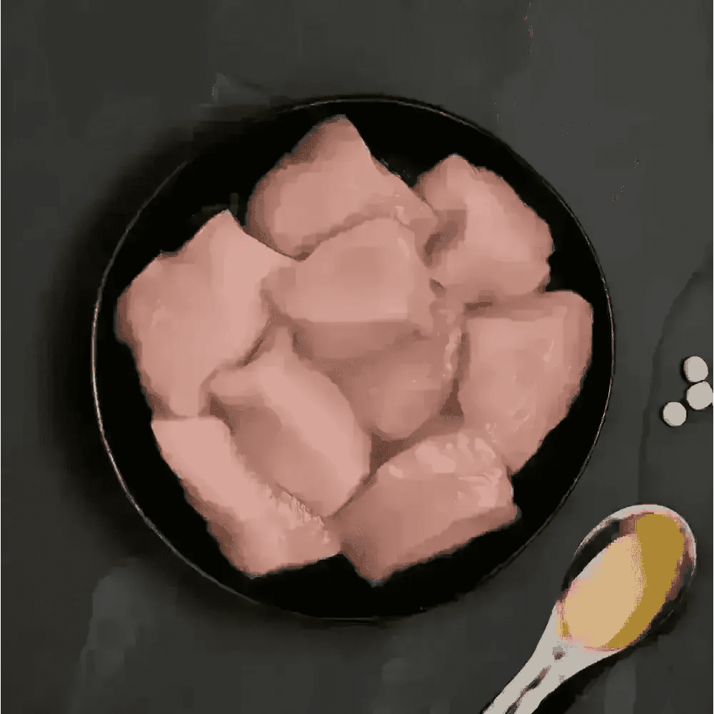 Raw chicken breast chunks in a black bowl with wooden spoon for fresh cat food