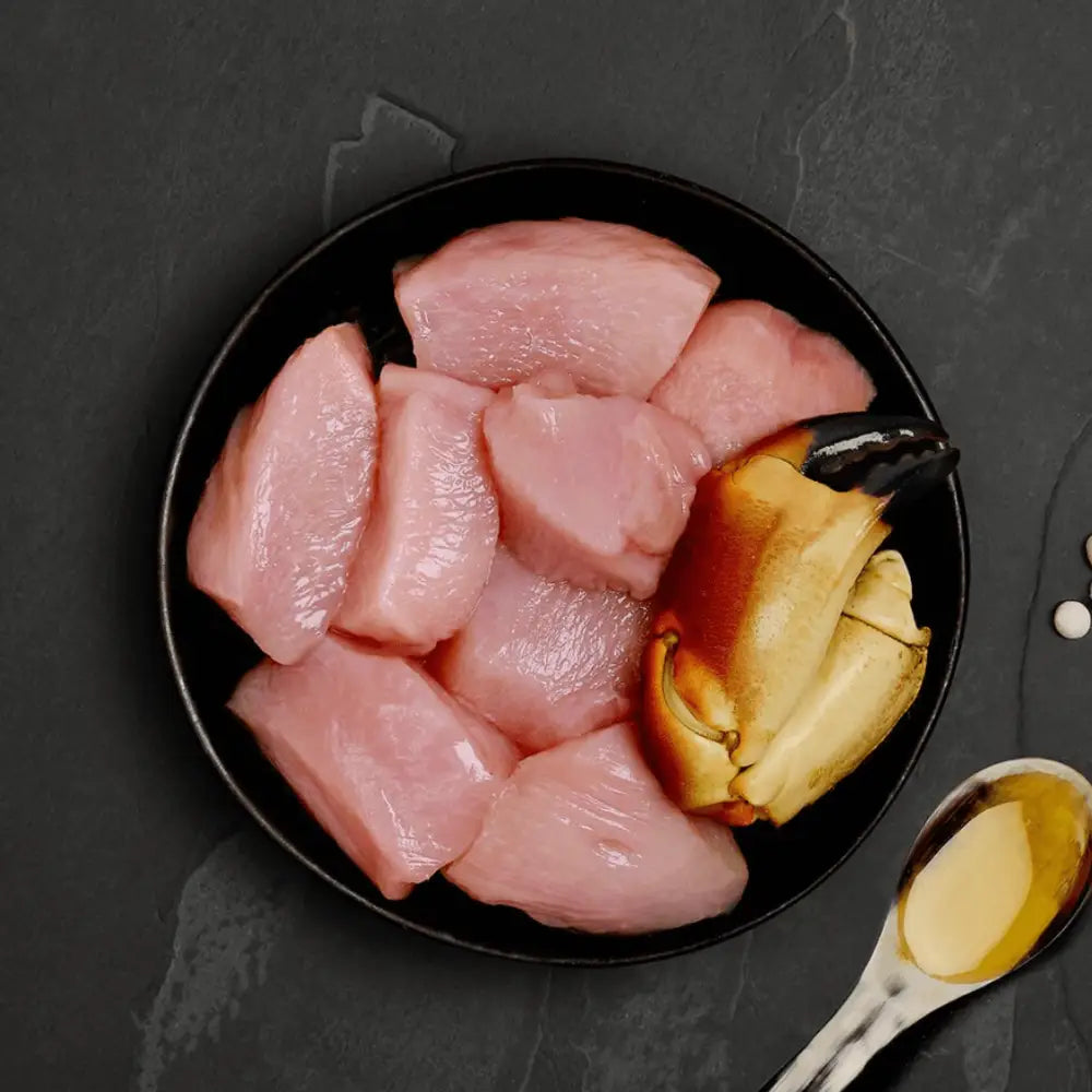 Black bowl with raw chicken pieces and soy sauce, part of Canagan Cat Food Can Chicken with Crab, a highly nutritious complete cat food