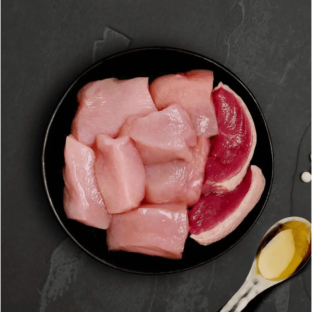 Black plate with raw chicken and beef slices with oil for Canagan Cat Food Can Chicken with Duck, a highly nutritious complete cat food to accompany dry food