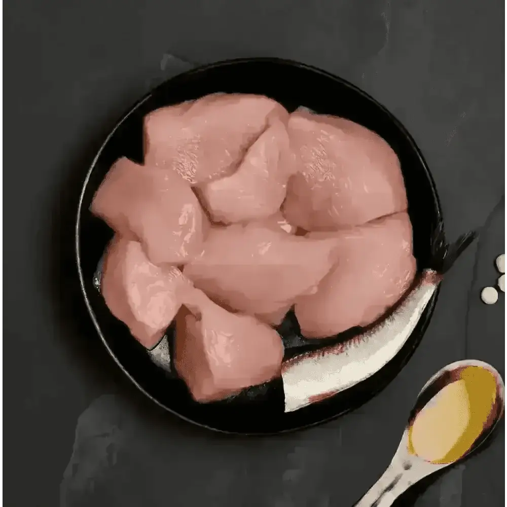 Black plate with raw chicken pieces, silver spoon, and salt shaker for Canagan Cat Food Can