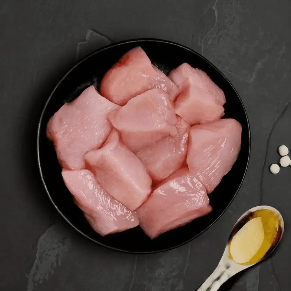Raw chicken breast chunks in a black bowl with wooden spoon for fresh cat food