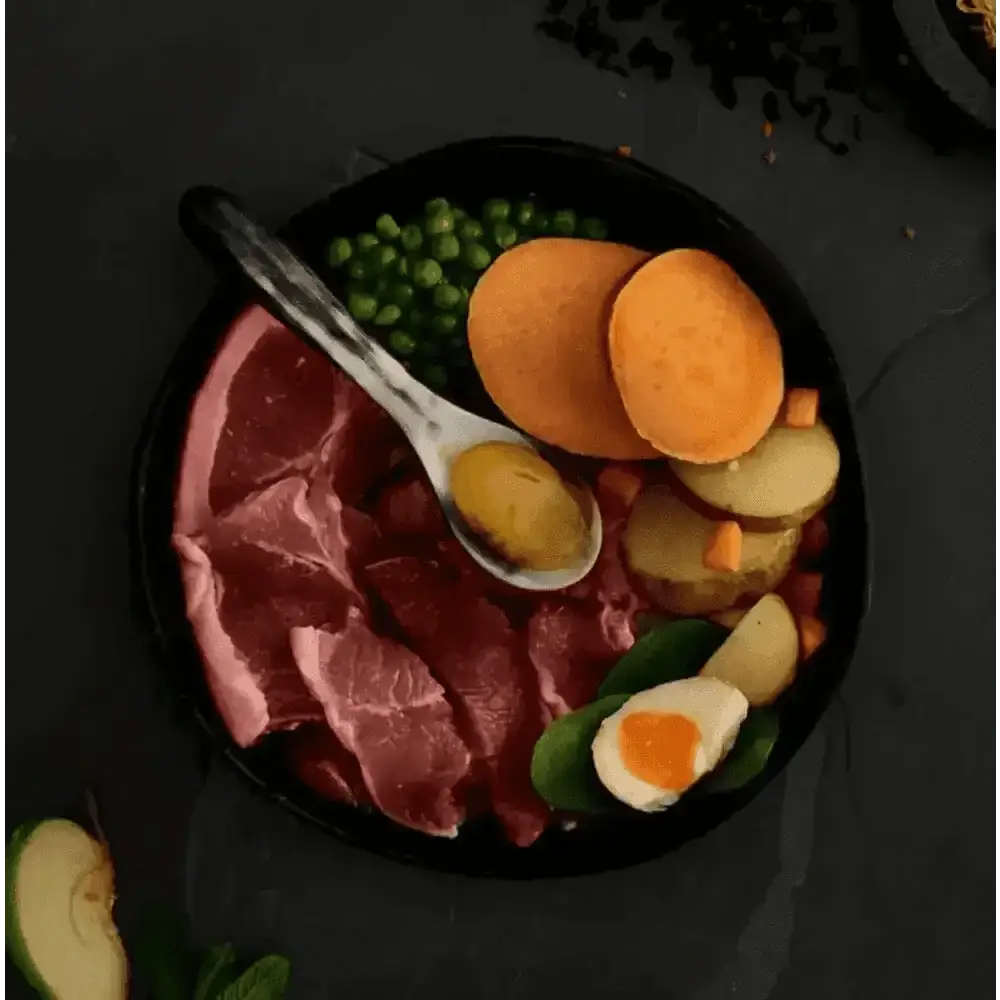 Black cast iron skillet with raw meat, vegetables, and eggs for grass fed dog food