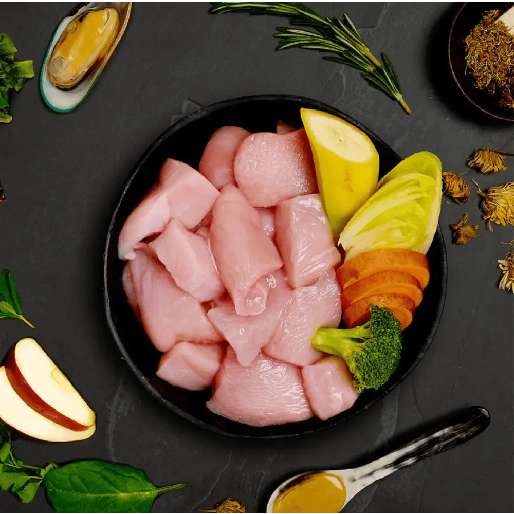 Black bowl with raw free run chicken, lemon slices, herbs, and spices for dog food