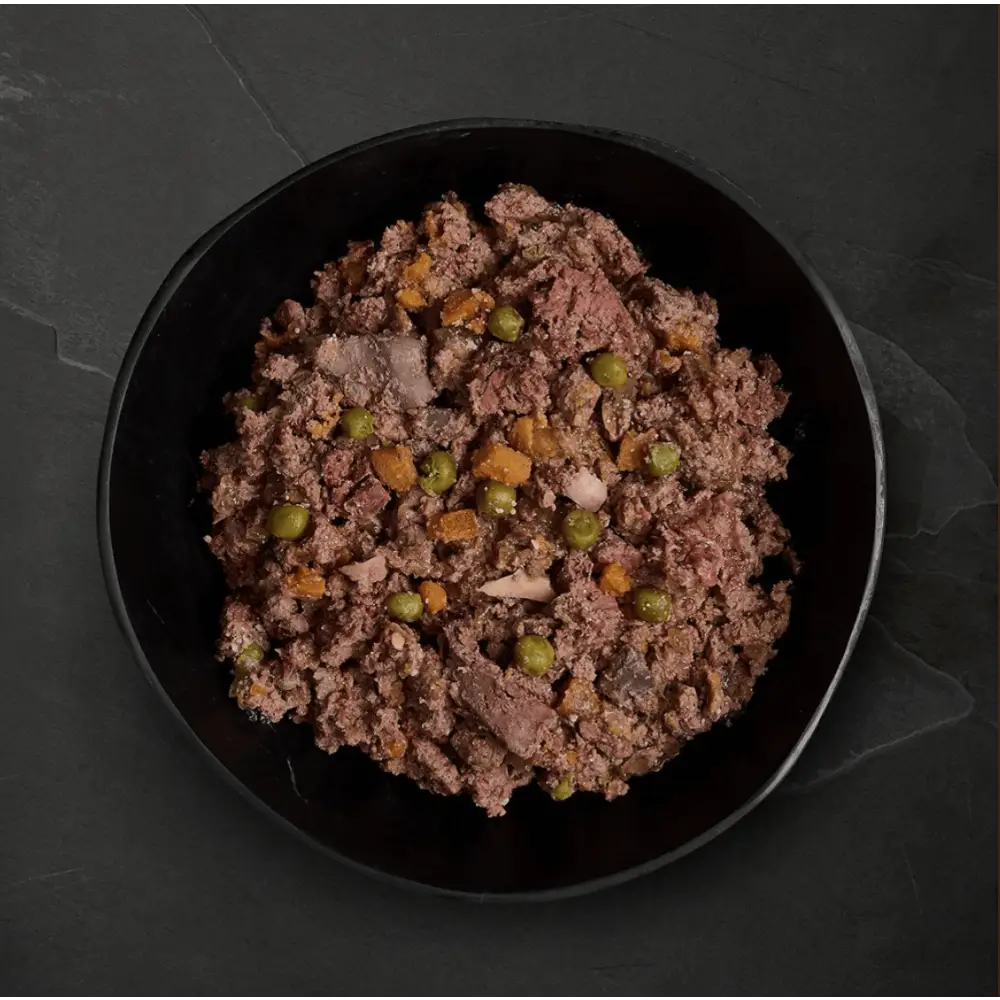 Black bowl with ground meat and peas from Canagan Wet Dog Food Variety Pack featuring freshly prepared deboned ingredients