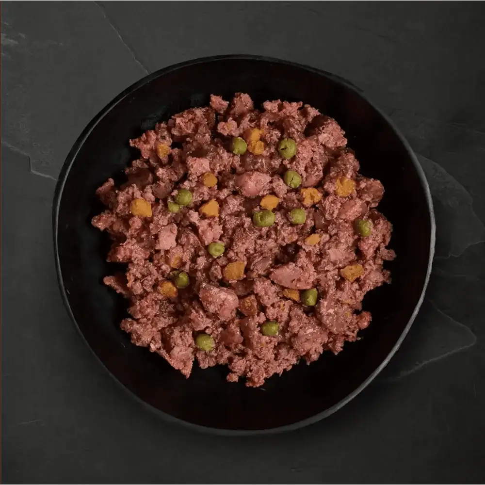 Black bowl with ground meat and peas from Canagan Wet Dog Food Variety Pack featuring freshly prepared deboned ingredients