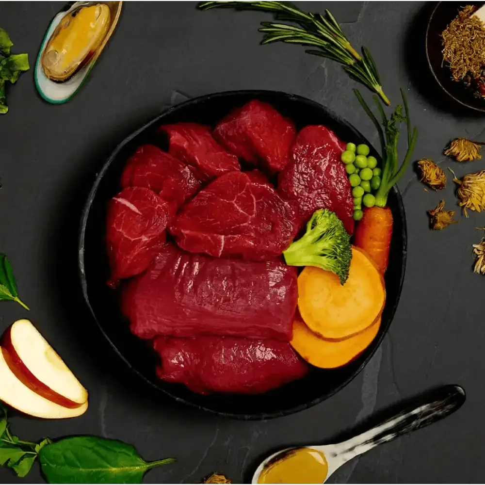 Black bowl with freshly prepared deboned beef slices, vegetables, and herbs for Canagan Wet Dog Food