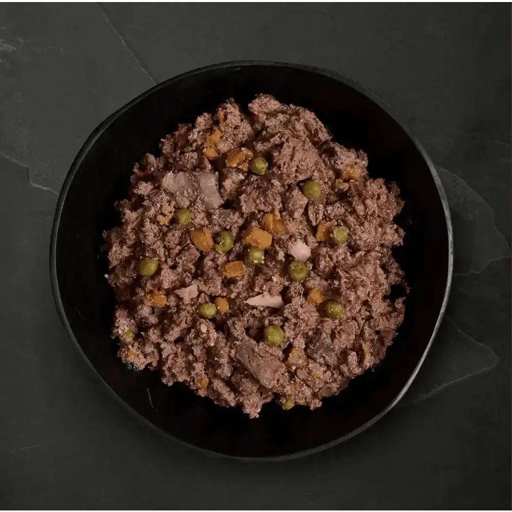 Black bowl with ground meat and peas from Canagan Wet Dog Food Variety Pack featuring freshly prepared deboned ingredients
