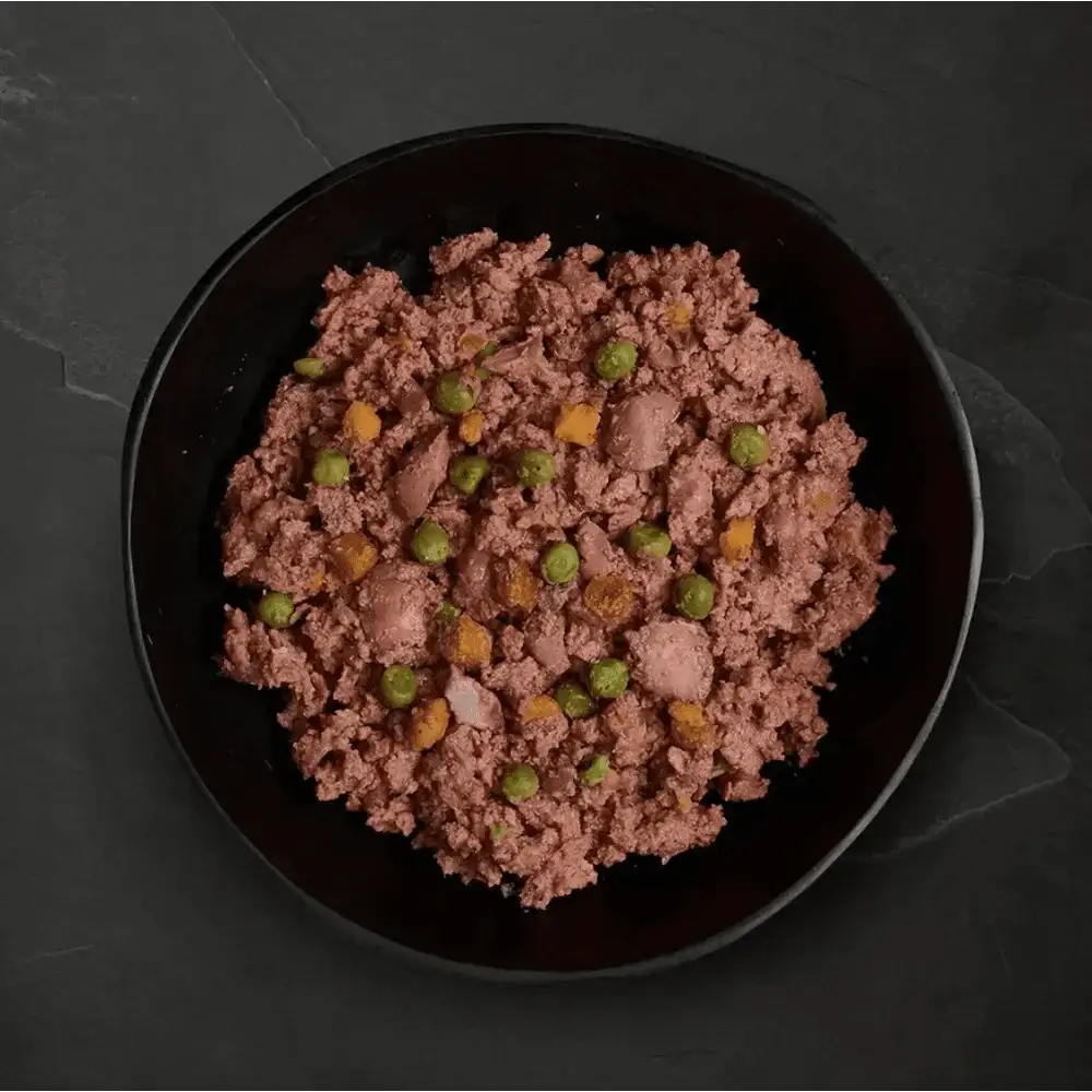 Black bowl with freshly prepared deboned dog food, pinkish food, green peas, corn, and brown bits