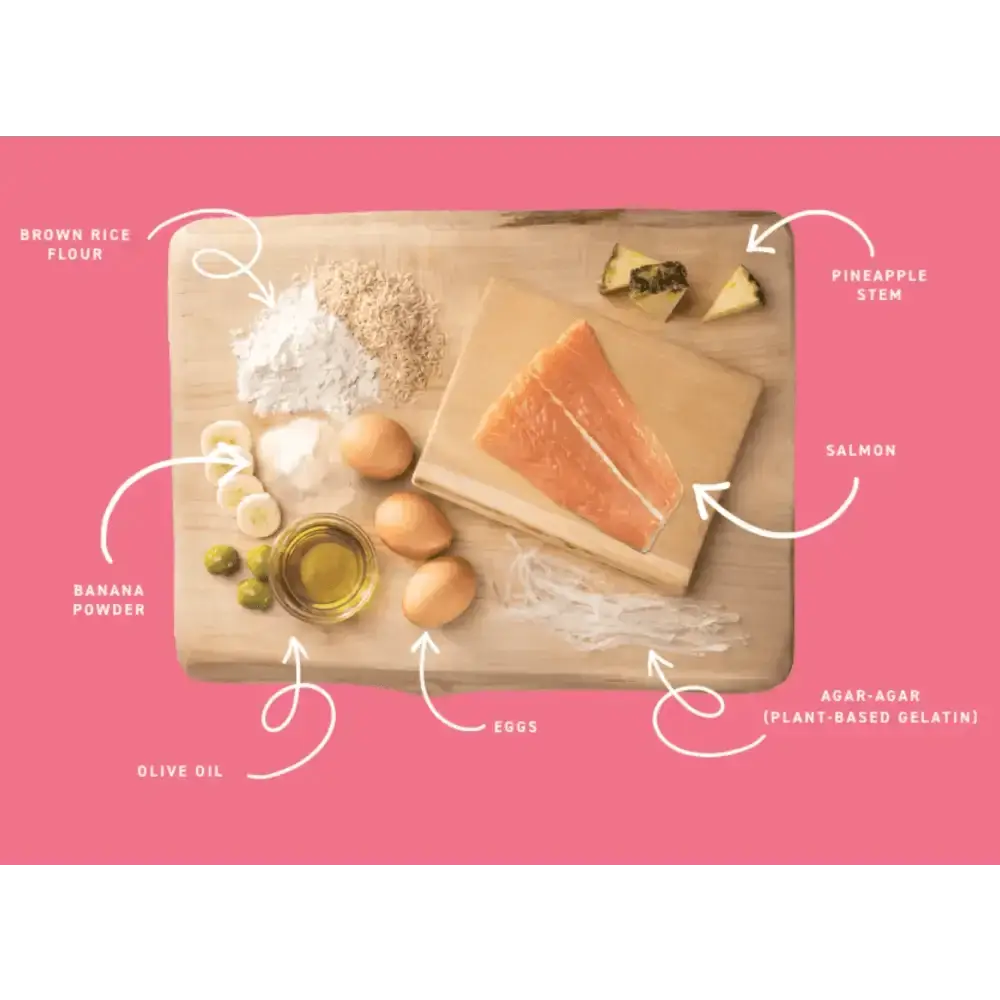 Wooden cutting board with salmon, eggs, olive oil, bananas, and pineapple slices for Earth Animal No-Hide Salmon Chew