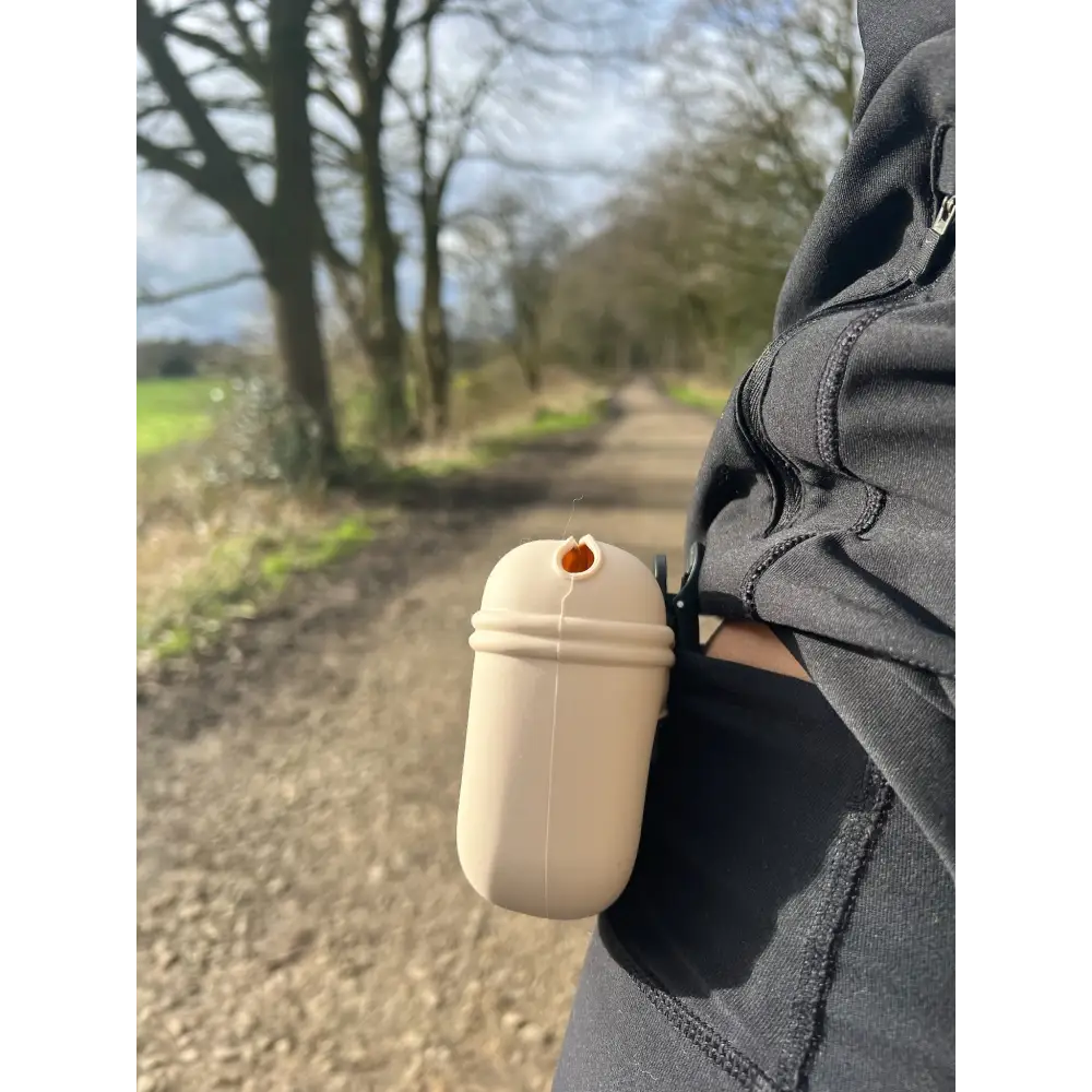 Beige silicone dog treat bag resembling coffee cup with orange opening