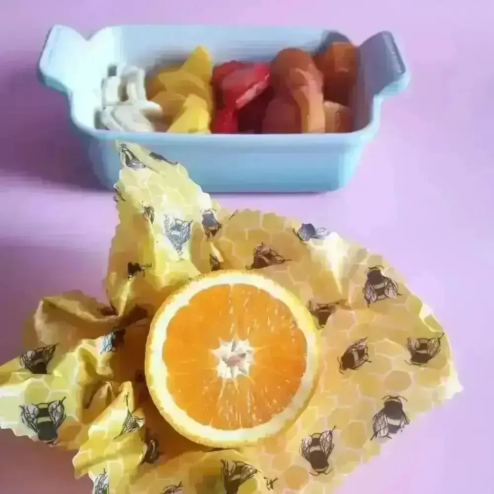 Orange slice on yellow beeswax wrap with black honey bee design