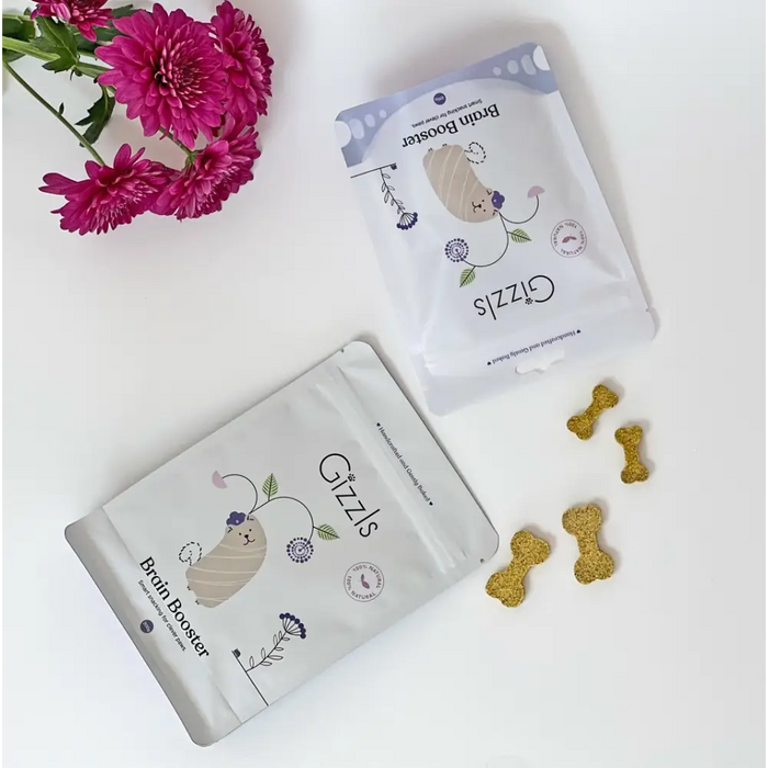 Two packages of 'Gizzls' brain booster treats for pets on a white surface with pink flowers.