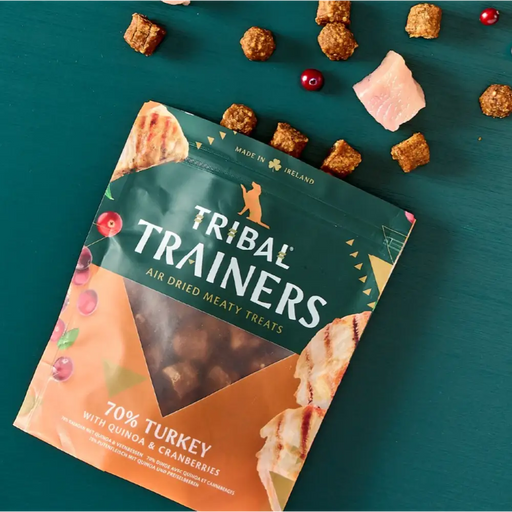 Packaging of Tribal Trainers dog treats on a teal background with treats scattered around.