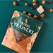 Packaging of Tribal Trainers dog treats on a teal background with treats scattered around.